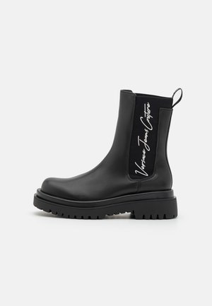 Black ankle boots made of smooth leather with a chunky sole, featuring elastic side panels and a pull tab, detailed with white branding.