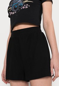 Black ribbed shorts with an elastic waistband, featuring a flowing design and subtle texture. The garment has an above-knee length.
