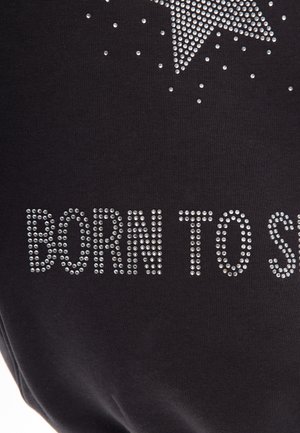 Schwarzer Textilstoff mit glänzenden Strasssteinen, die den Text "BORN TO SHINE" und ein Stern-Design bilden, wodurch eine strukturierte, reflektierende Oberfläche entsteht.