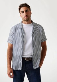 Camisa de manga corta con cuello, con un patrón geométrico azul y blanco, confeccionada en tela texturizada; presenta un cierre frontal con botones y un bolsillo en el pecho.