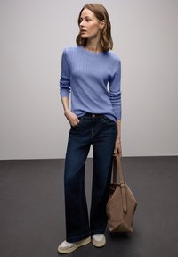 Lichtblauwe geribbelde trui, donkerblauwe jeans met wijde pijpen, beige handtas en lichte sneakers. De outfit heeft een casual, gestructureerd ontwerp.