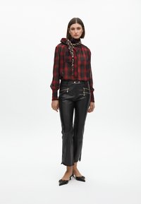 Červená a čierna kockovaná blúzka s šatkou okolo krku, v kombinácii s hladkými čiernymi koženými nohavicami s vytahovacími zipsami a čiernymi lodičkami s špičatou špičkou.