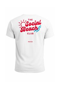 Weißes Baumwoll-T-Shirt mit rotem und blauem Text, der "THE Social Beach CLUB" liest, ergänzt durch Sonnen- und Wellen-Grafiken.