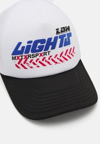 Cappellino da baseball bianco con una visiera nera strutturata. Presenta un grande testo blu e rosso, insieme a una grafica rossa che ricorda le impronte degli pneumatici.