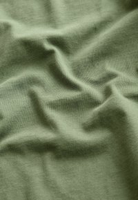 Svetlozelená látka, jemne textúrovaná s viditeľnými záhybmi a skladmi, vyrobená z elastického materiálu, ktorý poskytuje hladký vzhľad.