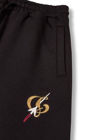 Schwarze Jogginghosen aus weichem Stoff, mit einem gestickten Logo-Design in Gold und Weiß mit einem roten Akzent und einer Seitentasche.
