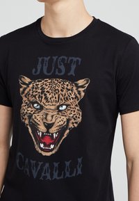 Černé tričko s grafikou bující hlavy leopardu a textem "JUST CAVALLI" nad a pod obrázkem.