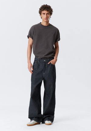 Graues T-Shirt mit kurzen Ärmeln, kombiniert mit lockeren, dunkelblauen Jeans. Die Jeans haben ein klassisches Fünf-Taschen-Design und eine minimalistische Optik. Bequeme Schuhe sind ebenfalls dabei.