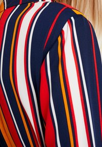 Tissu rayé avec des couleurs rouge, orange, blanc et bleu marine. Texture lisse avec des lignes verticales et un design de col.