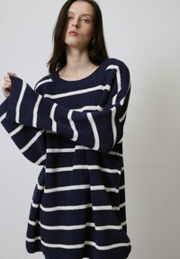 Pull oversized rayé bleu marine et blanc avec des manches larges, texture côtelée et poches latérales, accompagné d'un col rond.