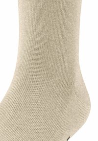 Calcetín beige hecho de tejido acanalado, mostrando una textura suave y un ligero brillo, con un talón redondeado y sin patrones visibles ni herrajes.