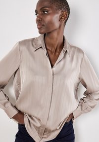 Camicia beige setosa con strisce verticali, colletto a risvolto e maniche lunghe, caratterizzata da una vestibilità rilassata e orlo curvo.