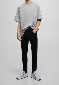 Camiseta gris de algodón con mangas cortas, combinada con jeans ajustados negros y zapatillas blancas. Diseño sencillo, sin patrones o detalles destacables.