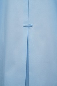 Φωτεινό γαλάζιο ύφασμα με κεντρική κάθετη σχισμή που συγκρατείται κλειστή από ένα οριζόντιο ραμμένο βρόχο πάνω από τη σχισμή.