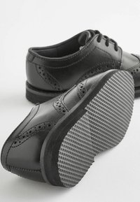 Chaussures en cuir noir avec des détails perforés et des orteils ronds. Semelles en caoutchouc plates avec une texture antidérapante. Design à lacets.