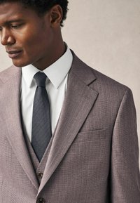 Grau strukturiertes Sakkos mit Reverskragen, weißem Hemd und dunkler gemusterter Krawatte. Slim Fit mit einer Brusttasche und einem Zwei-Knopf-Verschluss.