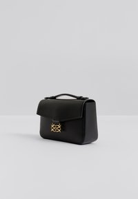 Μαύρο δερμάτινο τσάντα χειρός με δομημένο σχήμα, που διαθέτει εμπρόσθιο καπάκι και κούμπωμα με χ ρυσό μεταλλικό στοιχείο. Απλός σχεδιασμός με χειρολαβή στο πάνω μέρος.