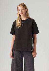 Tricou negru cu mânecă scurtă și decolteu rotund, realizat dintr-un material moale din bumbac. Croit lejer, asociat cu blugi negri evazați.
