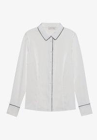 Camicia bianca a maniche lunghe con colletto classico, caratterizzata da piping nero lungo il colletto e i polsini, e una chiusura con bottoni sul davanti. Texture liscia.