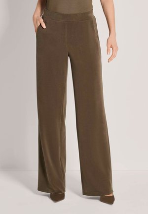 Vrouw die loszittende brede bruine broek met hoge taille en zijzakken draagt, gecombineerd met bruine puntige schoenen.
