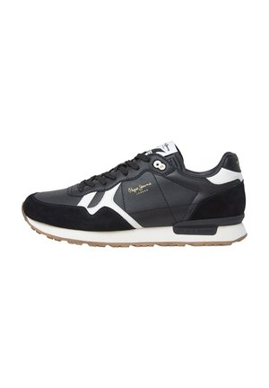 Zapatilla negra con materiales de ante y piel; presenta acentos blancos, una superficie texturizada y una suela de goma. Logo dorado en el lado.