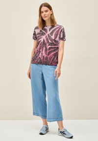 Kortärmad topp med ett rosa och svart abstrakt mönster, kombinerad med ljusblå vida jeans. Materialet tycks vara mjukt och lätt.