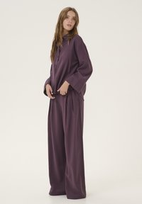 Purple loose-fitting top with long sleeves and button closure, paired with wide-legged pants made of smooth, lightweight material.