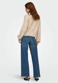 Hellbeige gestrickter Pullover mit fallenden Schultern, kombiniert mit weit geschnittenen blauen Jeans und schwarzen Absatzsandalen. Rückansicht.