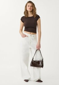 Smeđi pružni crop top, bijele široke traperice i mala tamnosmeđa kožna torba sa zaobljenim oblikom i kratkom drškom.