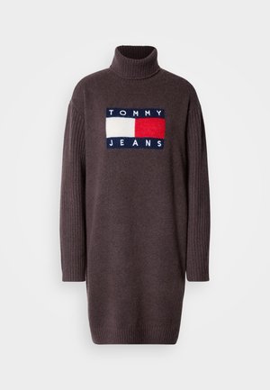 Haljina od ugljenasto sive vune s rebrastim rolkom i dugim rukavima. Na prednjem dijelu ističe se upečatljiva zakrpa s logom u mornarsko plavoj, crvenoj i bijeloj boji.