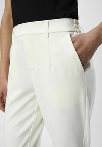Pantalones blancos a medida con una textura suave, que presentan un frente plano, bolsillos laterales y un diseño de cintura limpio.