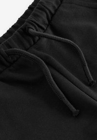 Svarta bomullsjoggers med elastisk midja och dragsko. Slät textur med insyddt tyg vid midjan för extra komfort.