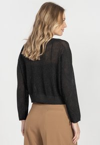 Czarny krótki sweter z teksturowanym splotem, prążkowanym wykończeniem i długimi rękawami. Materiał ma subtelny efekt połysku.