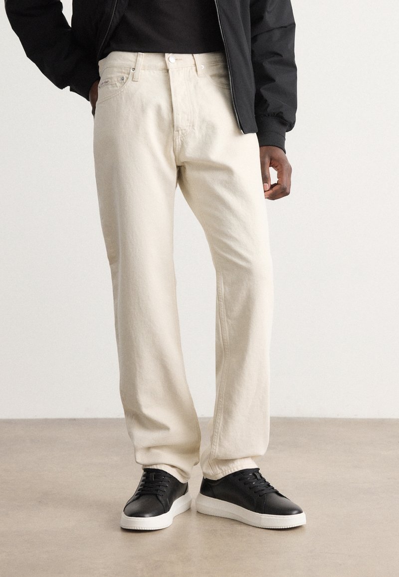 Světle béžové bavlněné kalhoty s volným střihem a rovnými nohavicemi. Doplněné černými koženými teniskami a černou bundou.