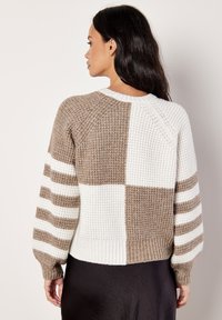 Sweter dzianinowy z wzorem w bloki w odcieniach beżu i bieli, z prążkowanymi rękawami i ściągaczem na dole. Przyjemny w dotyku, o skróconym kroju.