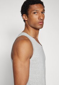 Graues Baumwolltanktop mit V-Ausschnitt, mit einer figurnahen Passform und glatter Textur, an einem Model im Profil dargestellt.