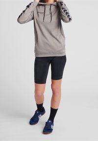 Ljusgrå hoodie med en texturerad design, accentuerad av svarta chevronränder på ärmarna. I kombination med svarta cykelbyxor och blå atletiska skor.