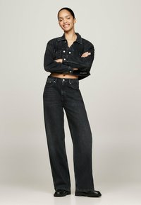 Chaqueta de mezclilla negra y jeans de pierna ancha con un diseño recortado, botones metálicos y detalles de textura sutil. Combinado con botas negras de tobillo.