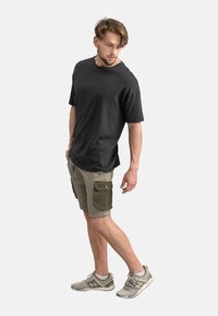 Zwarte katoenen T-shirt met korte mouwen, gecombineerd met licht khaki cargoshorts met twee zijzakken en donkergroene accenten. Grijze sneakers.
