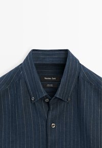 Marineblå linnedeskjorte med tynde hvide, lodrette nålestriber, knaplukket krave og forreste knapper fra Massimo Dutti.