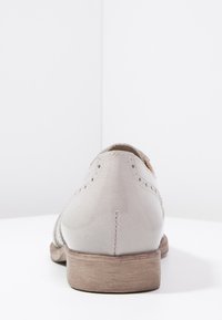 Chaussure en cuir gris clair avec un talon plat, présentant des détails perforés et des coutures le long de l'arrière. Design simple avec un talon incurvé.