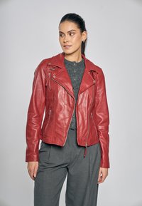 Rode leren motorjas met schuin geplaatste ritszakken, zilverkleurige accenten en een aansluitend ontwerp, gedragen met een grijs overhemd en grijze broek.