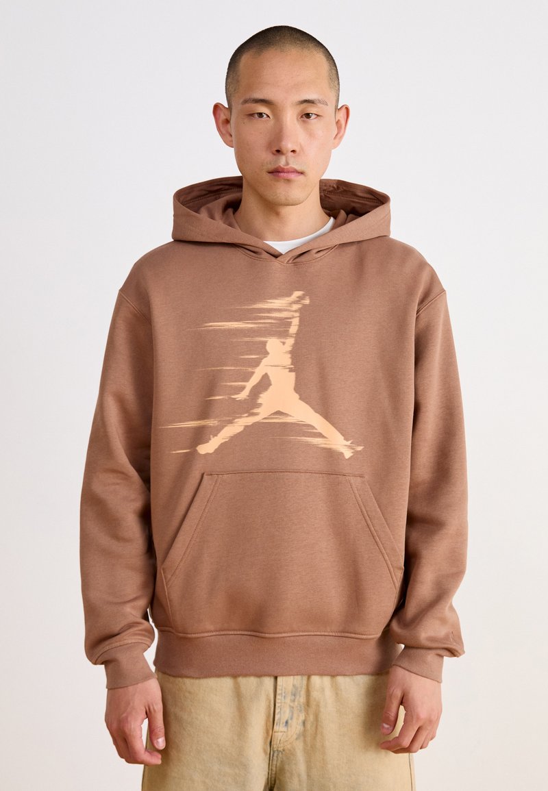 Sweat à capuche marron avec une poche kangourou, présentant un grand graphique beige clair d'une silhouette sautant sur le devant. Texture de tissu doux.