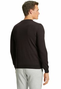 Maglione marrone lavorato a maglia con maniche lunghe, scollatura rotonda e polsini a coste, indossato sopra pantaloni grigi, visto da dietro.