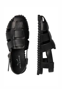 Sandalias de cuero negro con un diseño abierto, que presentan tiras trenzadas, una suela texturizada y cierre de hebilla lateral para un ajuste ajustable.