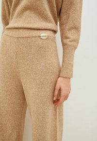 Pull en tricot beige et pantalon taille haute assorti, avec un poignet côtelé et un accent en métal au niveau de la ceinture. Texture douce.