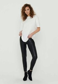 White, short-sleeve t-shirt paired with black, shiny leggings. The leggings are form-fitting, and the outfit is complemented by black ankle boots.