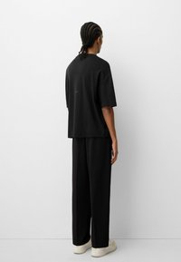 Tricou negru oversized cu croi lejer, maneci scurte și un branding subtil în spate, asortat cu pantaloni negri cu croi larg și teniși albi.