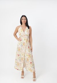 Robe maxi florale dans des couleurs pastel avec un design portefeuille et un col halter. Fabriquée en tissu léger, elle présente une fente haute sur la cuisse et une jupe fluide.