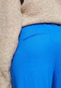 Jasnoniebieskie spodnie z miękkiego materiału, o prostym kroju i płaskiej kieszeni z tyłu, zestawione z beżowym, puszystym swetrem.